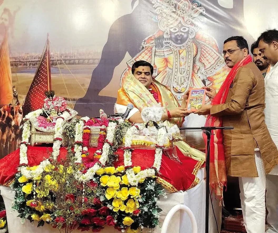 धार्मिक-सांस्कृतिक कार्यक्रम में मंच पर बैठे अतिथि को पुस्तक भेंट करते हुए विनोद कुमार उपाध्याय